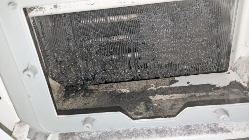 Mit grauem Flusenfilz komplett zugesetzte Kühlrippen des Kondensators durch die geschnittene Öffnung
