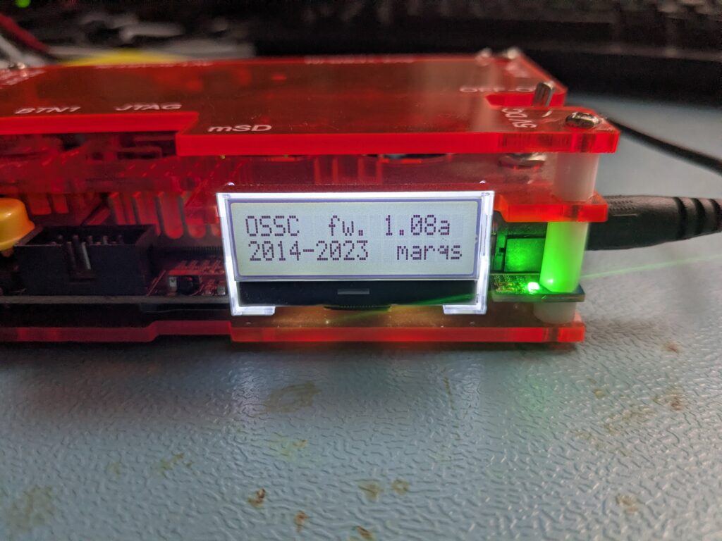 Nahaufnahme des OSSC LCD-Displays mit Bootscreen OSSC fw. 1.08a 2014-2023 marqs im roten Acrylgehäuse, daneben die Beschriftung mSD am Gehäuse