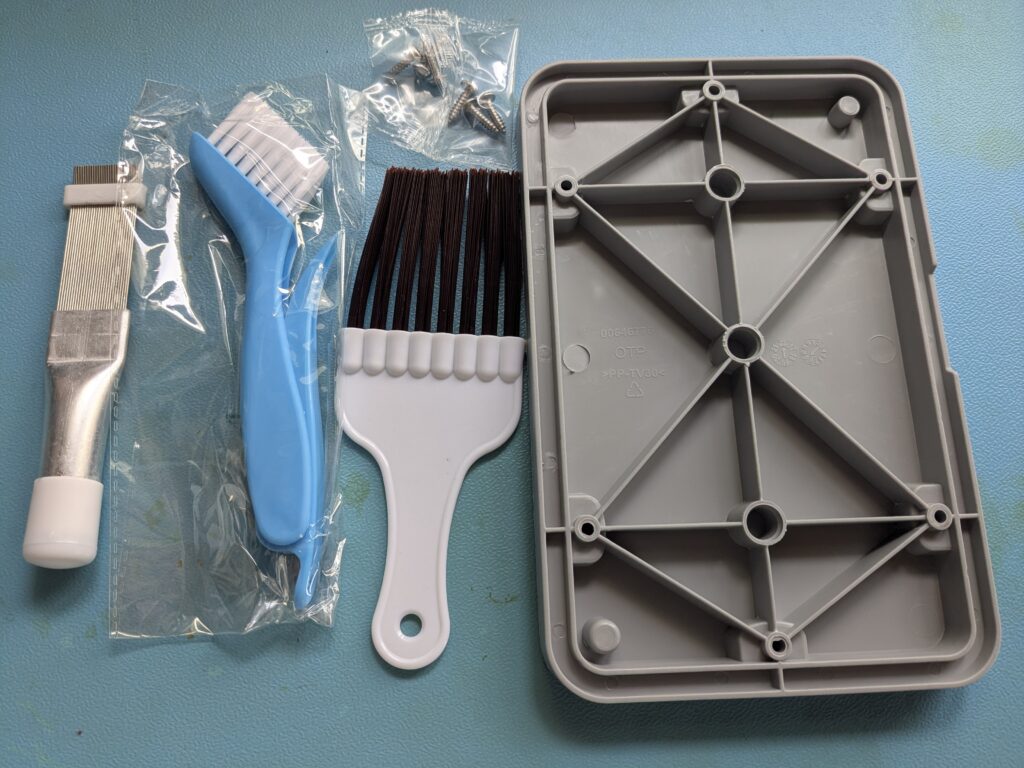 Gekauftes Reinigungsset mit Lamellenkamm, Bürsten, Schrauben und grauer Wartungsklappe