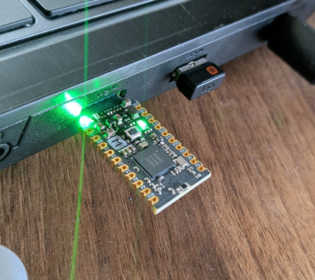 Das nRF52840-MDK-Dongle im USB-Port eines Notebooks, mit durchgehend grün leuchtenden LEDs im Bootloader-Modus.