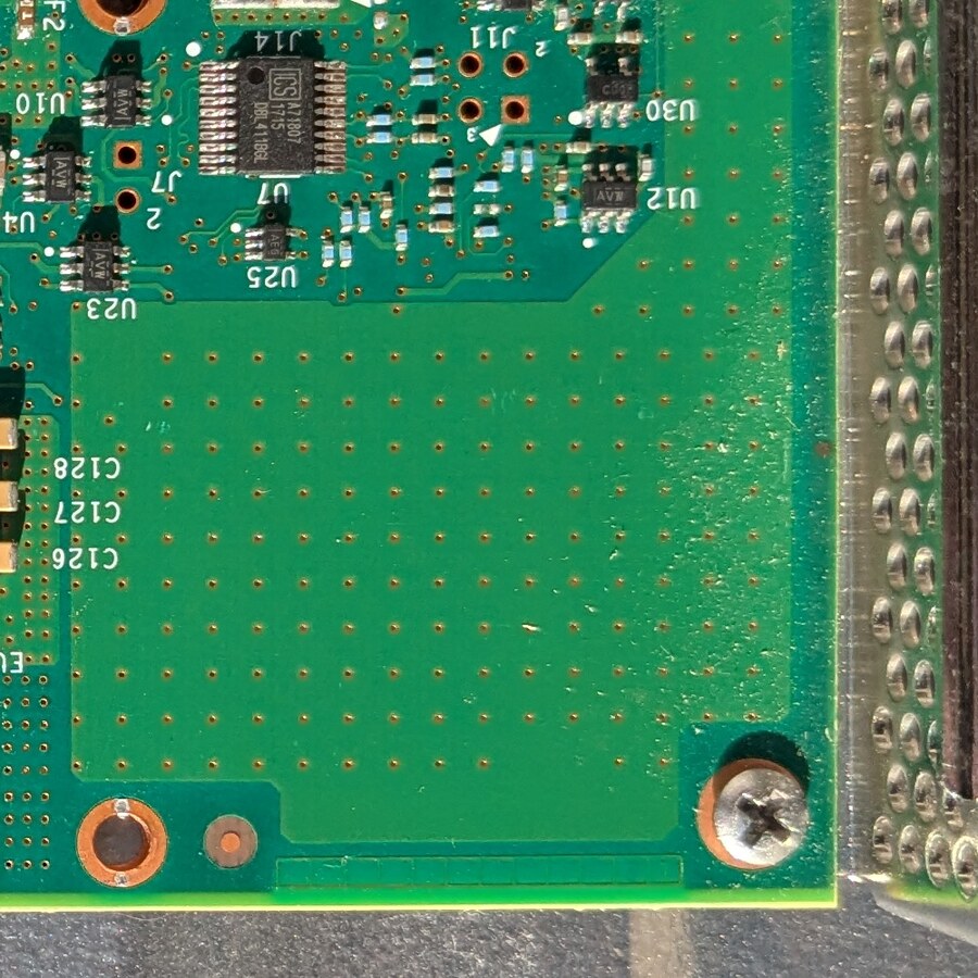 Nahaufnahme der unbestückten BGA-Lötfläche neben dem Slotblech des Intel QuickAssist Adapter 8950-SCCP, ein komplettes leeres Pad-Raster in Chipgröße