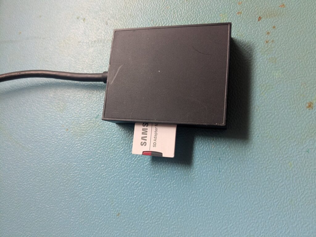 MicroSD-Karte im Samsung-Adapter, gesteckt in einen schwarzen USB-Kartenleser auf einer Küchenarbeitsplatte