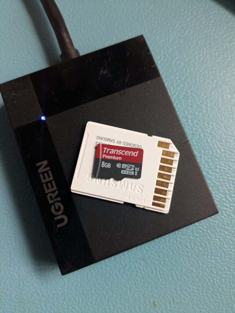 Transcend Premium 8GB microSDHC Class 10 U1 im Samsung-Adapter, liegend auf einem UGREEN-USB-Kartenleser mit blau leuchtender Status-LED