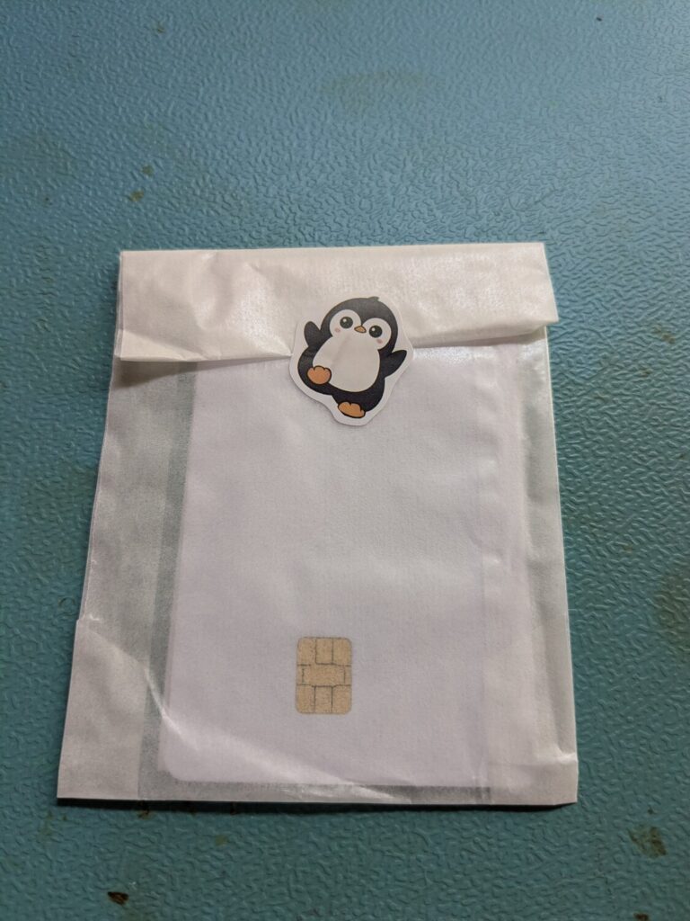 Weißer Versandumschlag mit Pinguin-Sticker, darunter die Chipkarte mit sichtbarem Goldchip.